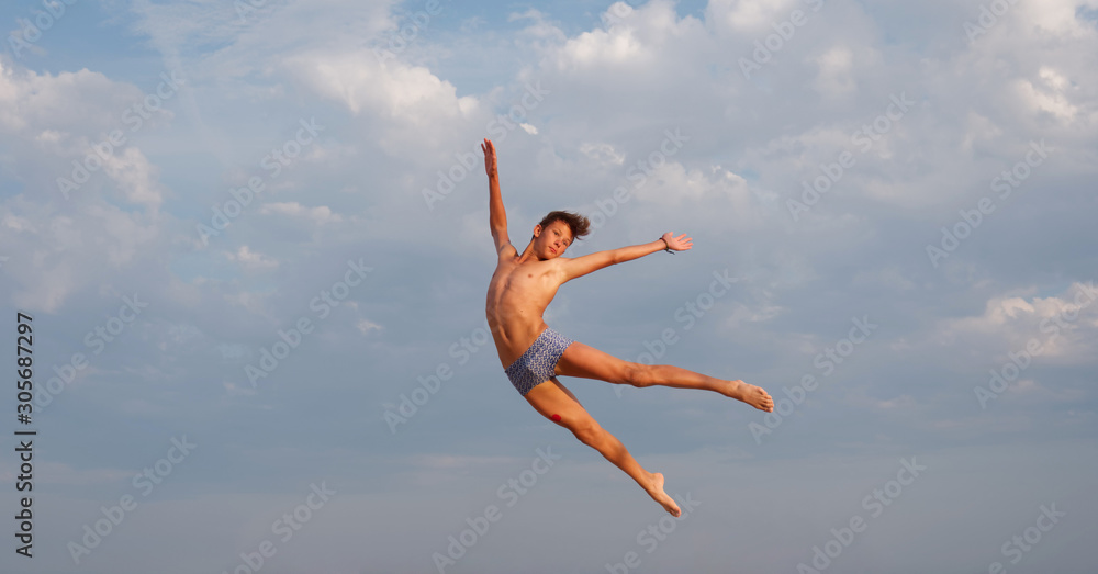 athletic teenager on the beach in jump on the background of the sea and sky