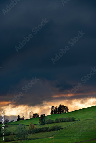 Green grass over hill during sunset with dramatic sky