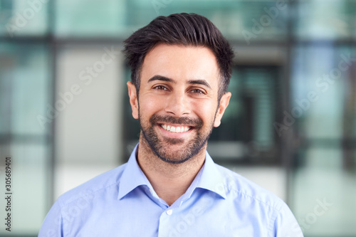 Portrait Of Smiling Businessman Standing In Lobby Of Busy Modern Office