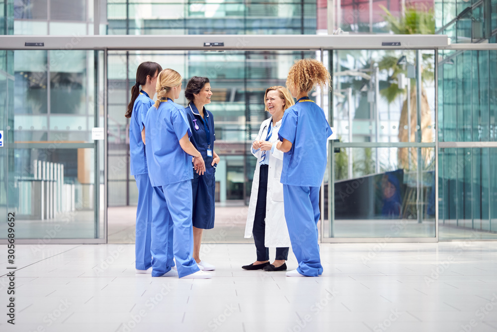 Female Medical Team Having Informal Meeting Standing In Lobby Of Modern Hospital Building Female Medical Team Having Informal Meeting Standing In Lobby Of Modern Hospital Building