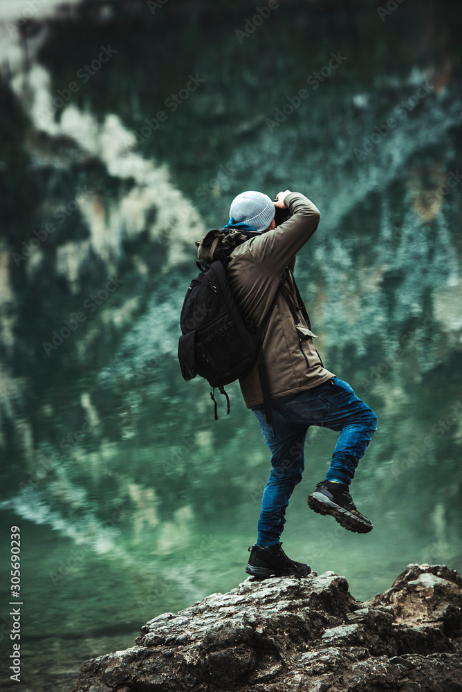 Obraz premium Male photographer standing on top of small rock in Lago di Braies (Braies lake, Pragser wildsee) during evening with reflection in water