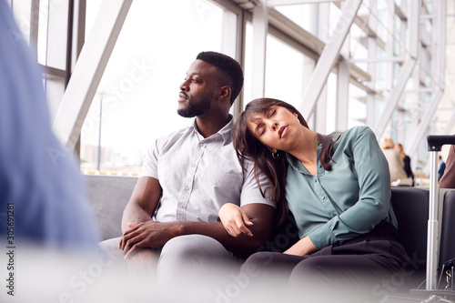 Tired Business Couple Sitting By Window Waiting In Airport Departure Lounge © Monkey Business