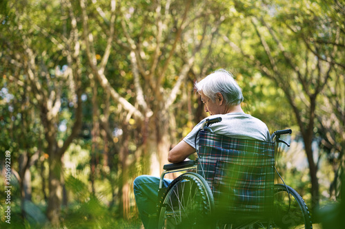 rear view of asian old man sitting in a wheelchair with head down looking sad and depressed photo