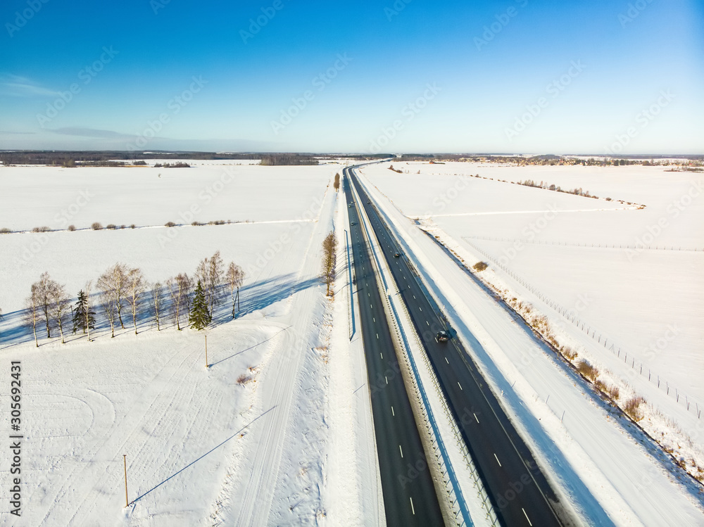 Beautiful aerial view of snow covered fields with a two-lane road among trees. Scenic winter landscape near Vilnius, Lithuania.