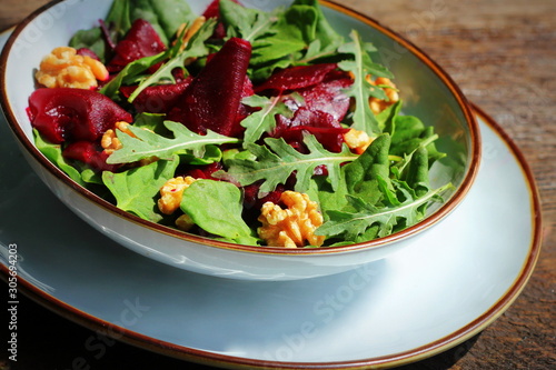 Healthy Beet Salad with fresh sweet baby spinach, arugula, nuts on wooden background