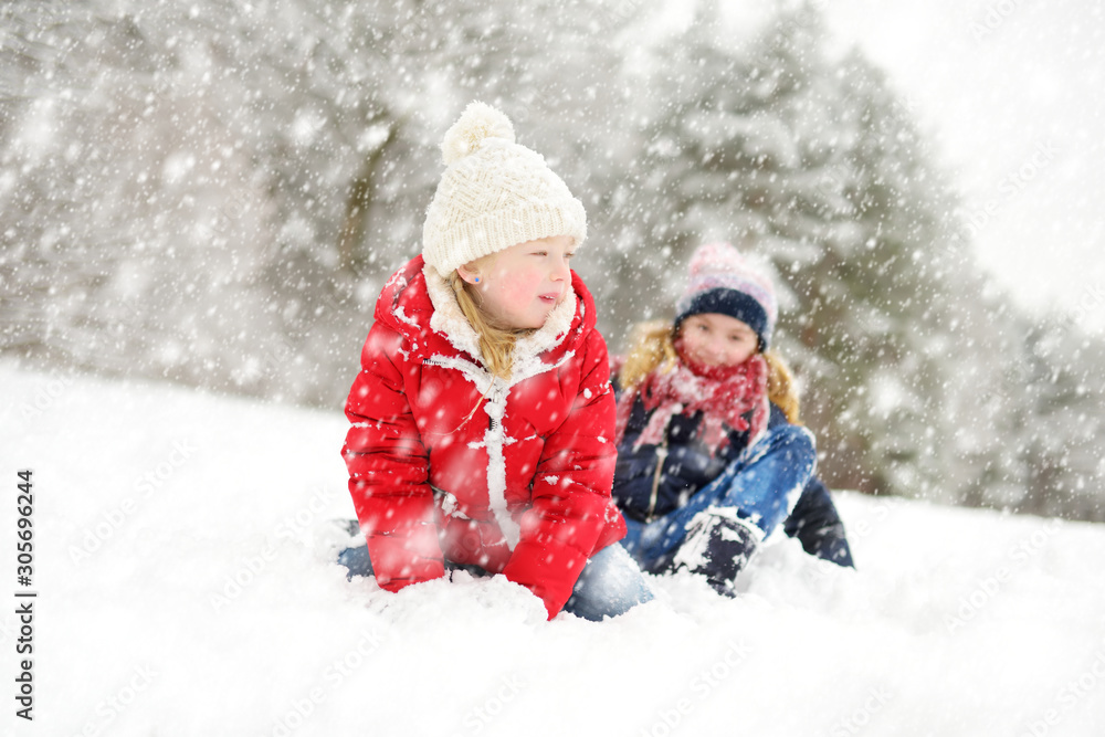 Two adorable young girls having fun together in beautiful winter park. Cute sisters playing in a snow. Two adorable young girls having fun together in beautiful winter park. Cute sisters playing in a snow.