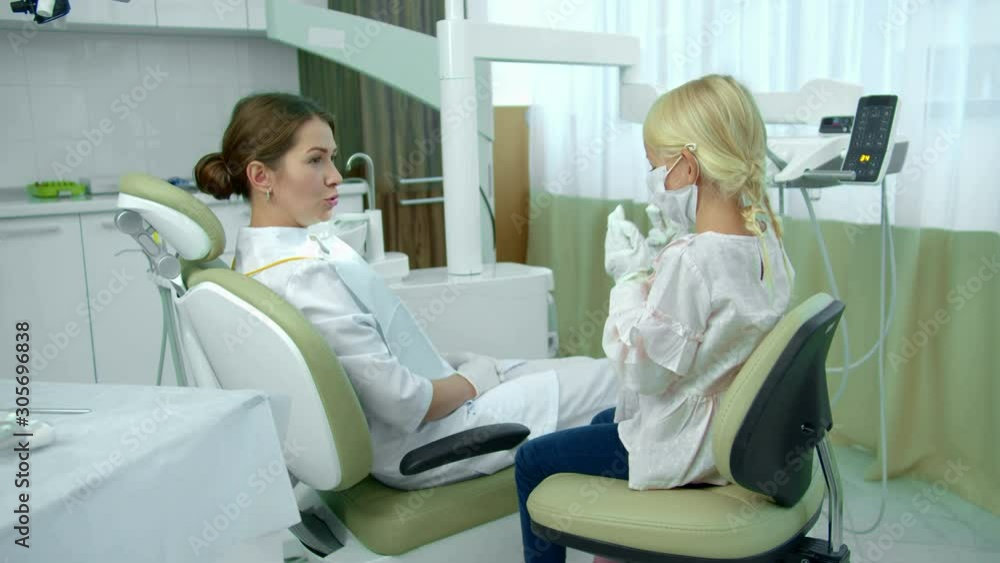 Dentist sits in patient chair and talks with girl Dentist sits in patient chair and talks with girl