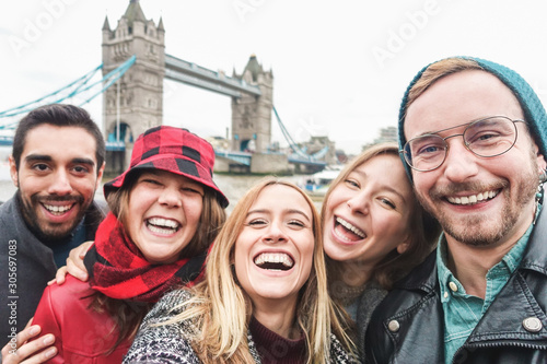 Happy friends taking selfie photo in london with Tower Bridge in background - Young people having fun with technology trends - Travel and friendship concept - Main focus on right guy face