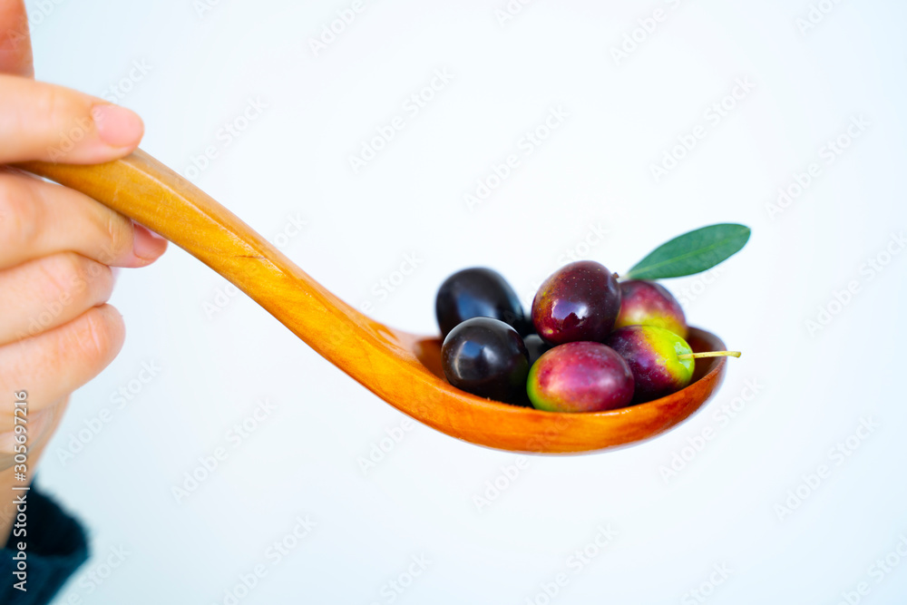 Fototapeta premium A woman handful of Mediterranean olives on a wooden spoon on isolated white background