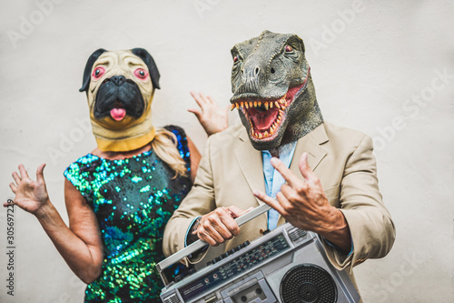 Crazy senior couple dancing for party wearing t-rex and chicken mask - Old trendy people having fun listening music with boombox stereo - Absurd and funny trend concept - Focus on dino face