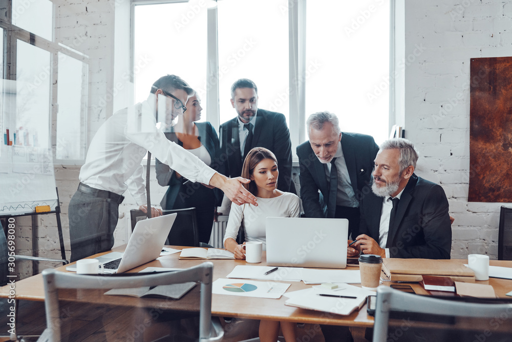 Professional business team analyzing sales using modern technologies while having staff meeting in the board room Professional business team analyzing sales using modern technologies while having staff meeting in the board room