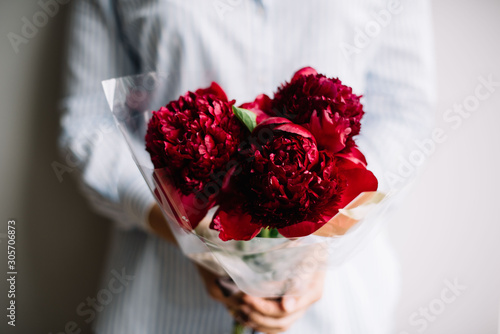 very nice young man holding a beautiful blossoming flower mono bouquet of fresh burgundy peonies on the grey wall background photo