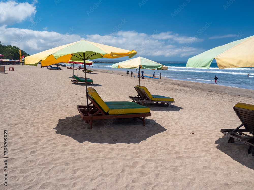 Kuta beach, Bali, november 2019: Sun umbrellas stay on yellow sand beach with blue sea and blue sky on background. Concept for rest, relaxation, holidays, spa, resort. Indonesia