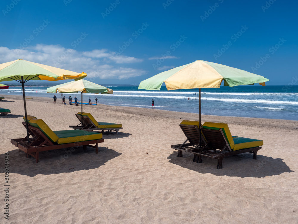 Kuta beach, Bali, november 2019: Sun umbrellas stay on yellow sand beach with blue sea and blue sky on background. Concept for rest, relaxation, holidays, spa, resort. Indonesia