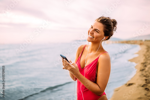 Beautiful young woman laughing and using her smartphone on the beach