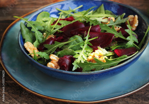Healthy Beet Salad with fresh sweet baby spinach, arugula, nuts in blue bowl on wooden background