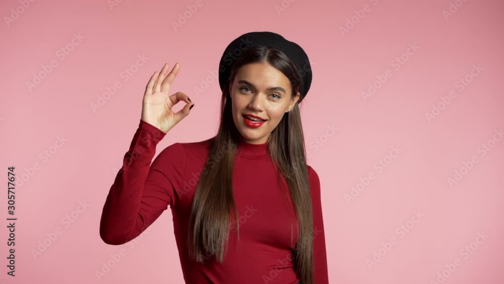 Winner. Success. Positive girl making thumbs up sign over pink background and smiles to camera. Body language. Young hipster woman with perfect red lips make-up and french hat. Winner. Success. Positive girl making thumbs up sign over pink background and smiles to camera. Body language. Young hipster woman with perfect red lips make-up and french hat.