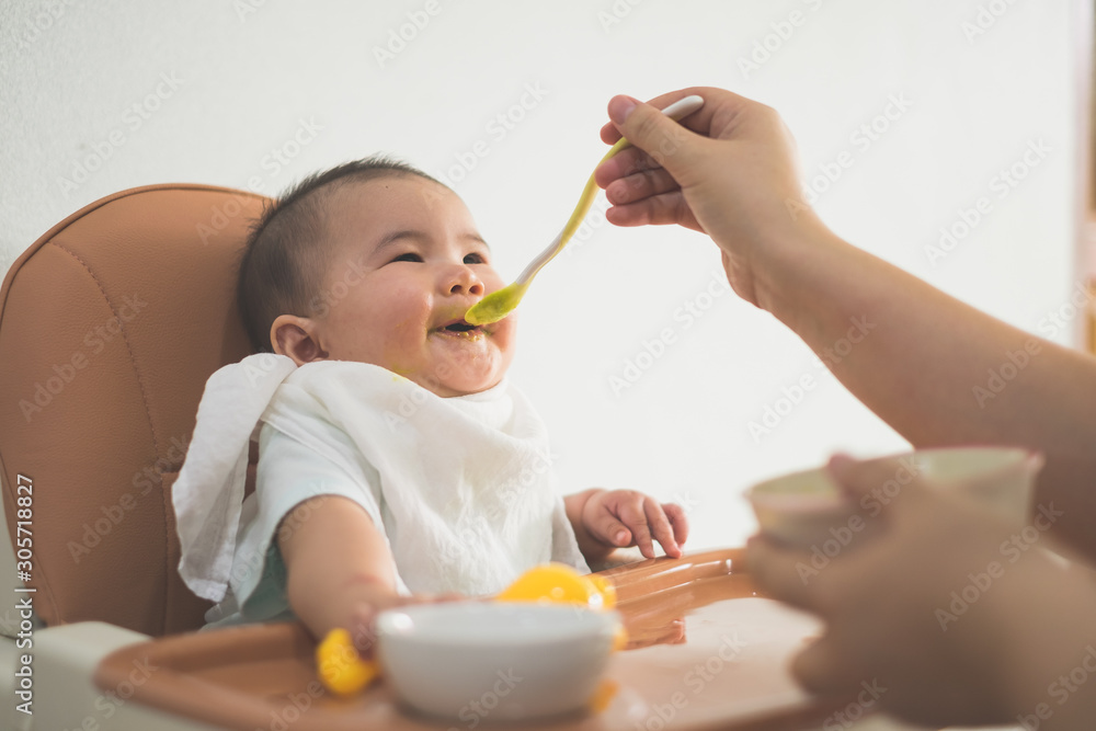 Young mother feeding her baby son with fruit puree Young mother feeding her baby son with fruit puree