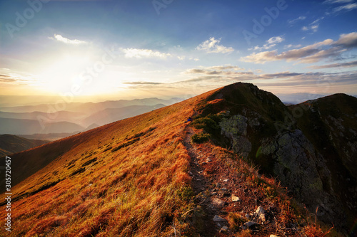 Beautiful sunset over the mountain peaks and hills panorama with vibrant yellow grass, autumn rural landscape with cloudy sky. Adventure mountain trekking. Beautiful moody light. Panoramic background