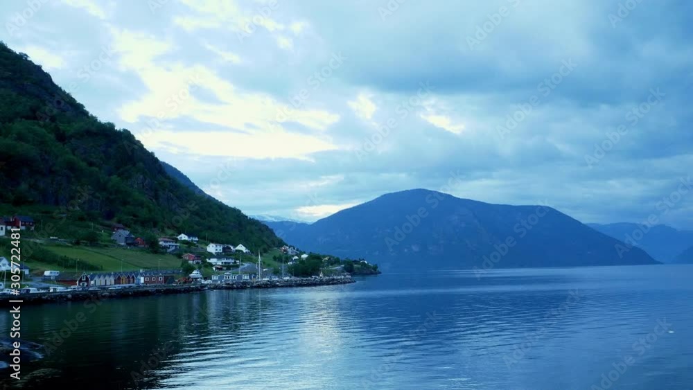 A picturesque village with traditional wooden houses at the base of a mountain along the shore of the Sognefjord in Norway, in an evening clip.