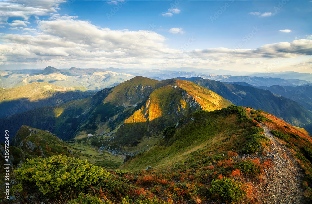 Fototapeta premium Hiking path in mountain peaks and hills panorama outdoor view, autumn rural landscape with cloudy sky. Adventure mountain trekking. Beautiful moody light. Panoramic background