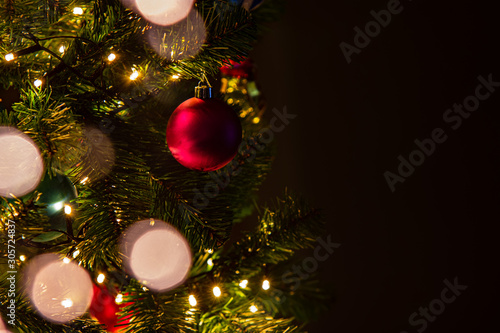 Closeup of Christmas tree with lights, balls and decorations, dark background