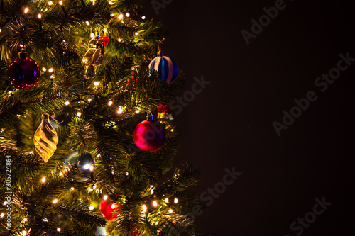 Closeup of Christmas tree with lights, balls and decorations, dark background