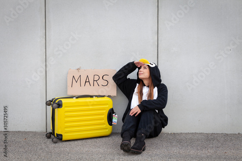 Young woman, with penguin costume and yellow suitcase, has to travel due to global warming. Symbolizes a sad penguin who has to leave his homeland because of global warming or climate change. photo