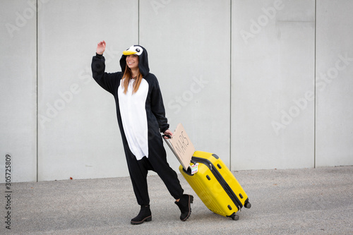 Young woman, with penguin costume and yellow suitcase, has to travel due to global warming. Symbolizes a sad penguin who has to leave his homeland because of global warming or climate change. photo