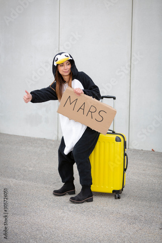 Young woman, with penguin costume and yellow suitcase, has to travel due to global warming. Symbolizes a sad penguin who has to leave his homeland because of global warming or climate change. photo