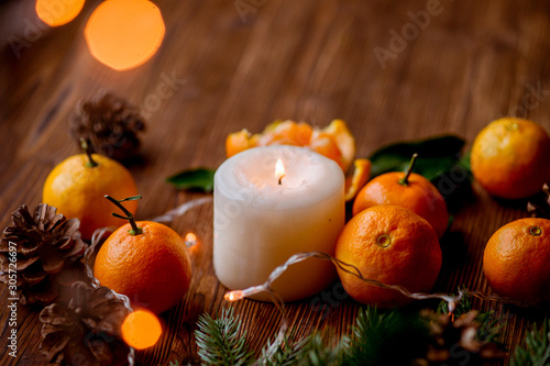 tangerines  candle  lights  cones  tree branch on a wooden background