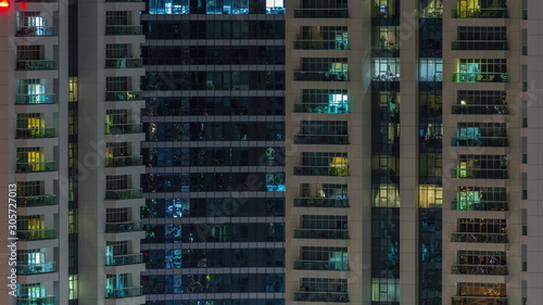 Rows of glowing windows with people in apartment building at night.