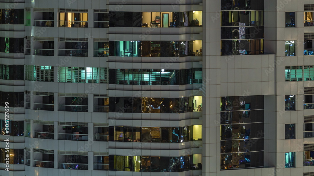 Rows of glowing windows with people in apartment building at night.