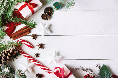 Beautiful Christmas composition on white background with golden Christmas gift boxes, snowy fir branches, conifer cones, holiday decoration and red berry. Top view