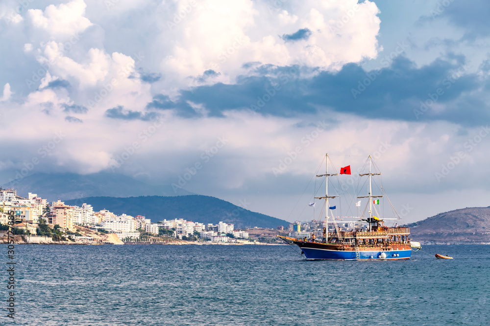 Obraz premium Vintage mast wooden sailing ship for sea tours in port of Saranda, Albania with red state albanian flag with black double-headed eagle, and italian flag and The Flag of Europe or European Flag