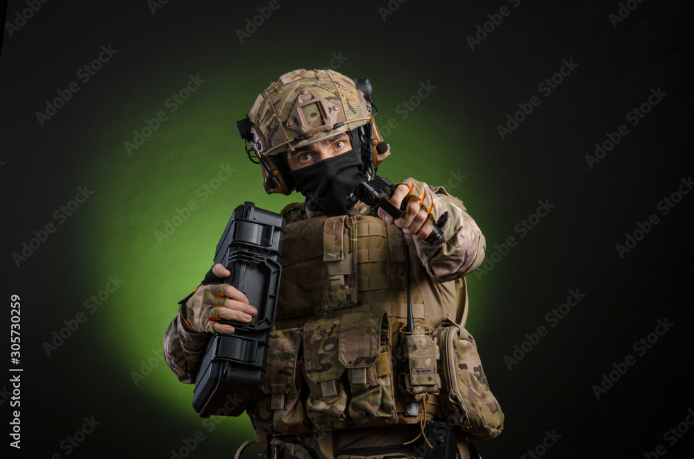 Fototapeta premium a male soldier in military clothes with a weapon on a dark background