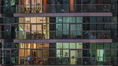 Rows of glowing windows with people in apartment building at night.