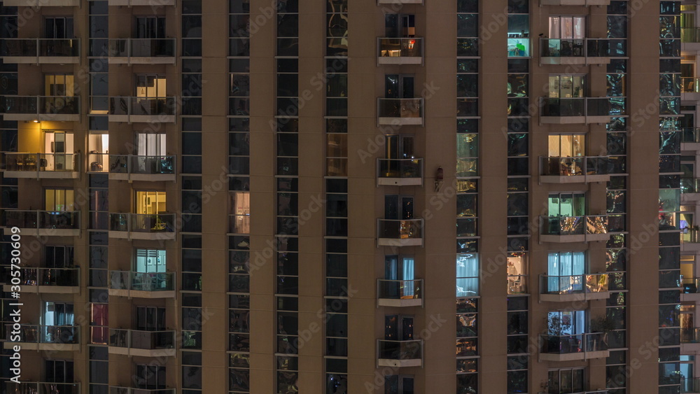 Rows of glowing windows with people in apartment building at night.