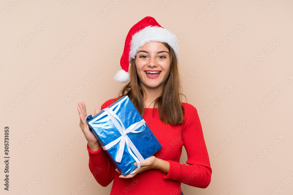 Young girl with christmas hat holding a gift over isolated background Young girl with christmas hat holding a gift over isolated background