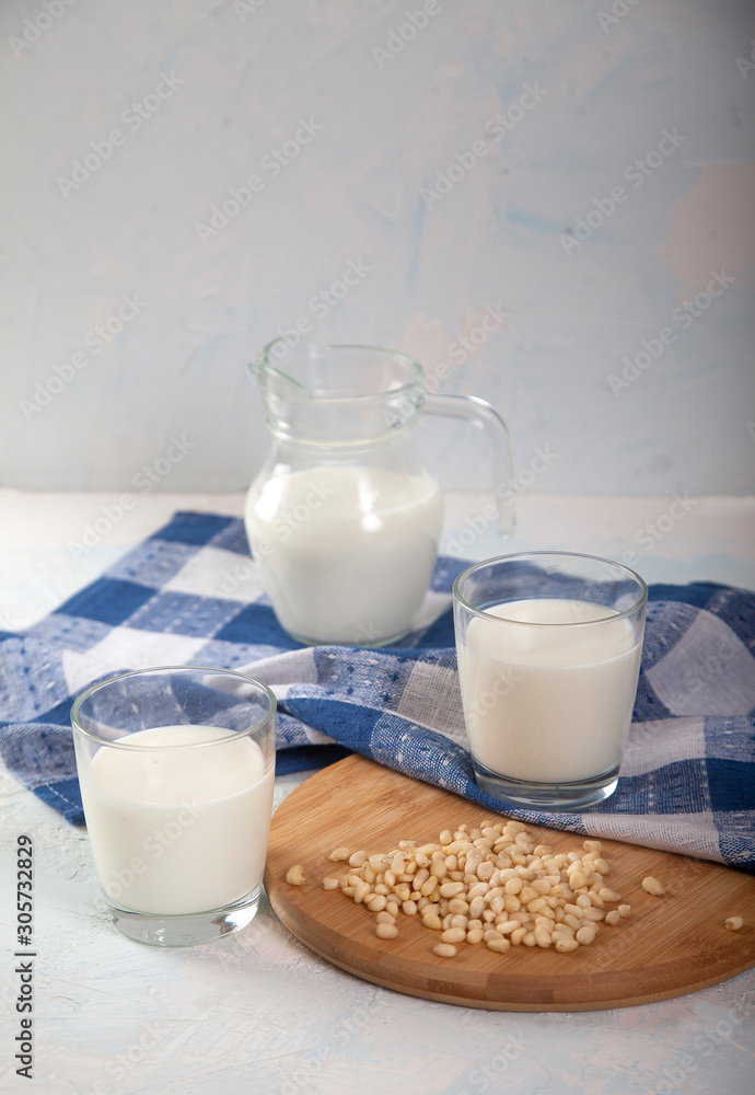 Vegetarian pine nut milk in glass cups and jug and blue linen napkin on white background. Vertikal. Vegetarian pine nut milk in glass cups and jug and blue linen napkin on white background. Vertikal.