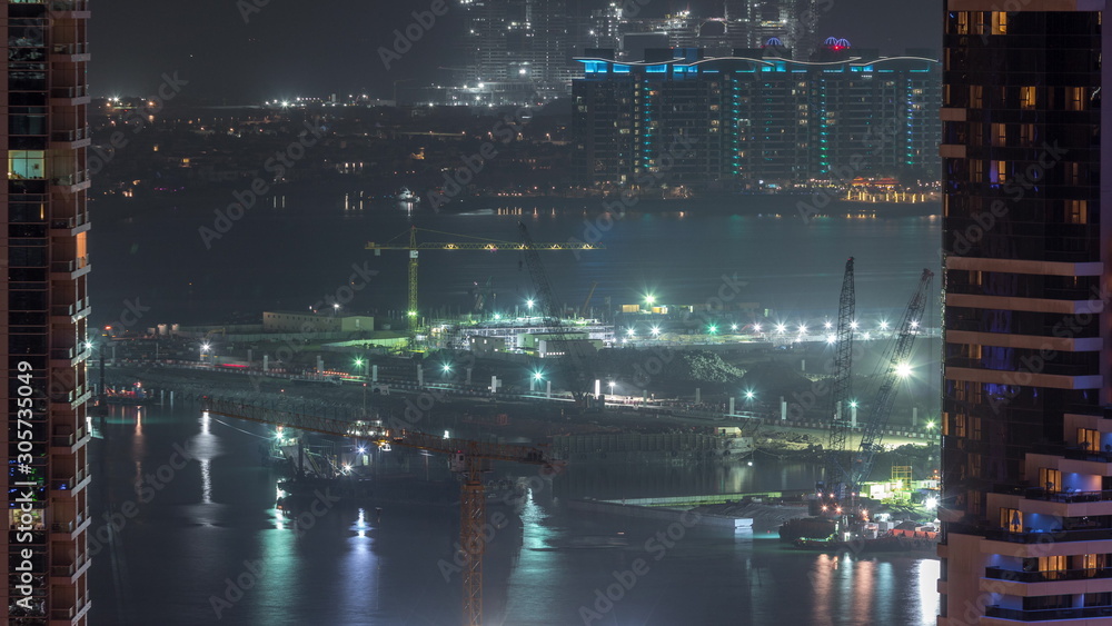Aerial view to Dubai marina skyscrapers with construction site and Palm Jumeirah Island on background night timelapse.
