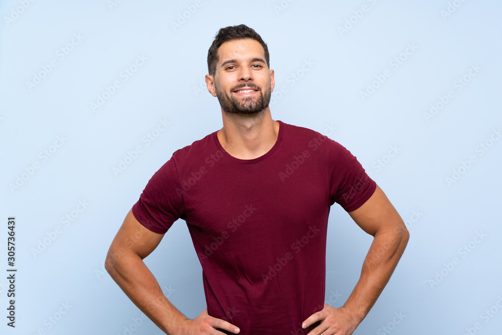 Handsome man over isolated blue background posing with arms at hip and smiling Handsome man over isolated blue background posing with arms at hip and smiling