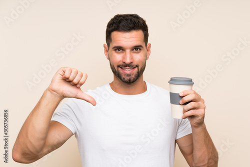 Young man with beard holding a take away coffee over isolated blue background proud and self-satisfied