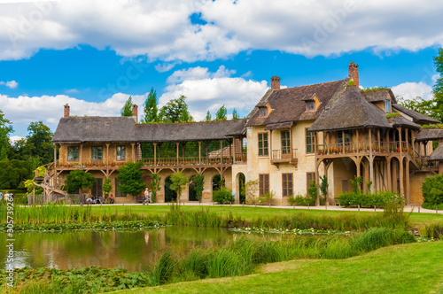 Lovely panoramic view of the Queen’s House and the adjoining Réchauffoir in the Hamlet of the Trianon gardens in Versailles. The two rustic buildings are connected by a covered gallery.