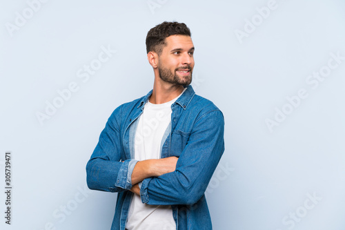 Handsome man over isolated blue background with arms crossed and happy