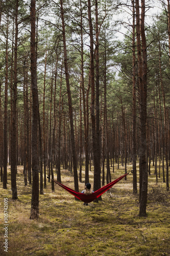 Woman relaxing in the hammock hanging among the pine trees in the background.