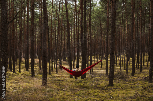 Woman relaxing in the hammock hanging among the pine trees in the background.