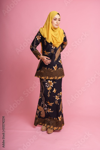 Beautiful female model wearing black "baju kurung" batik design with hijab, a modern lifestyle outfit for Muslim woman isolated over pink background. Eidul fitri fashion and beauty concept.