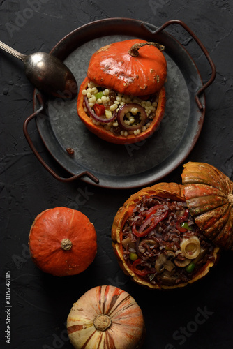Healthy vegan food. Small pumpkins stuffed with red rice, mushrooms, leek, peppers, ptitim and raisins on vintage metal tray on black background