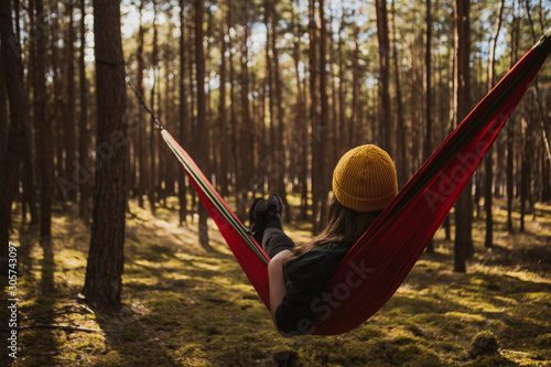 Beautiful young woman relaxing in hammock in forest. Summer scenery, a beautiful morning in the bosom of nature. The girl admires the views and nature. Breathed fresh air. Beautiful morning light. © Lukasz
